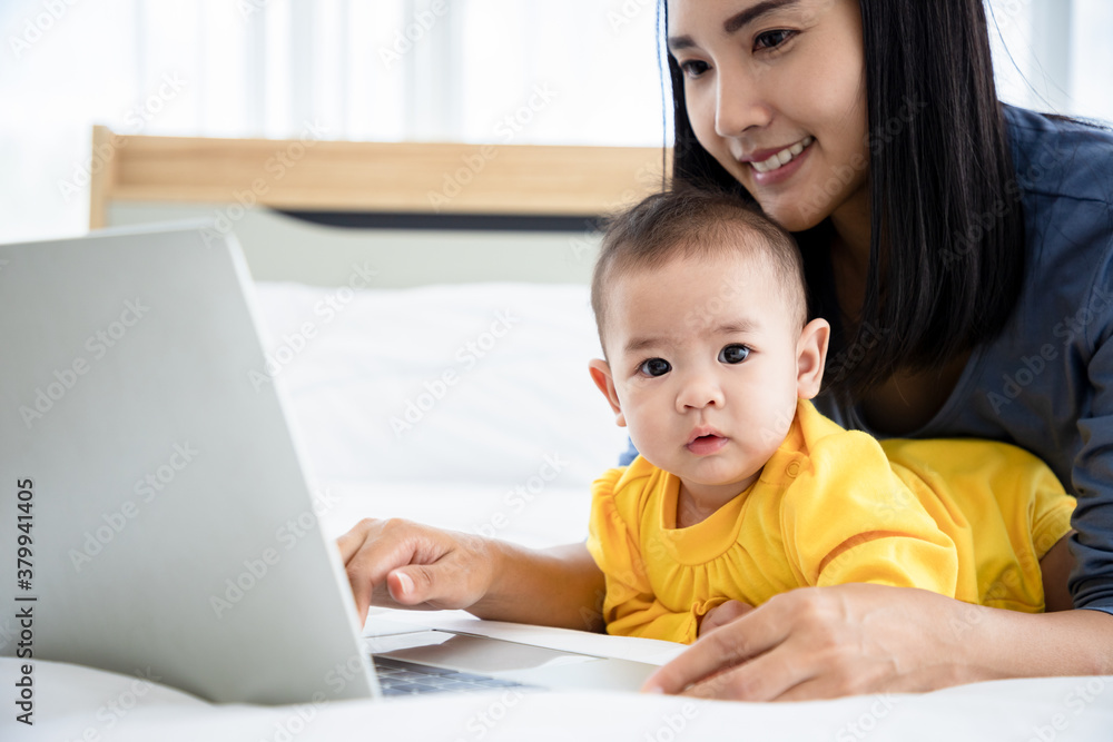 Young mother paly and searching data via laptop for baby daughter on the bed. Take care and help concept. Young mother paly and searching data via laptop for baby daughter on the bed. Take care and help concept.