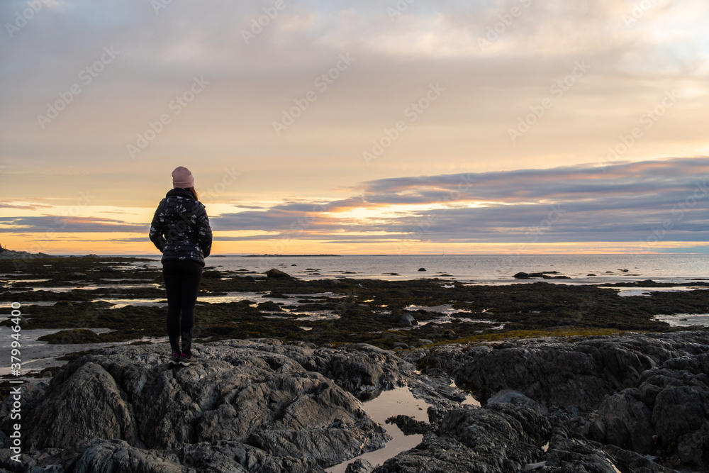 Back view of a woman admiring a colorful sunrise in the Bic national park, Canada