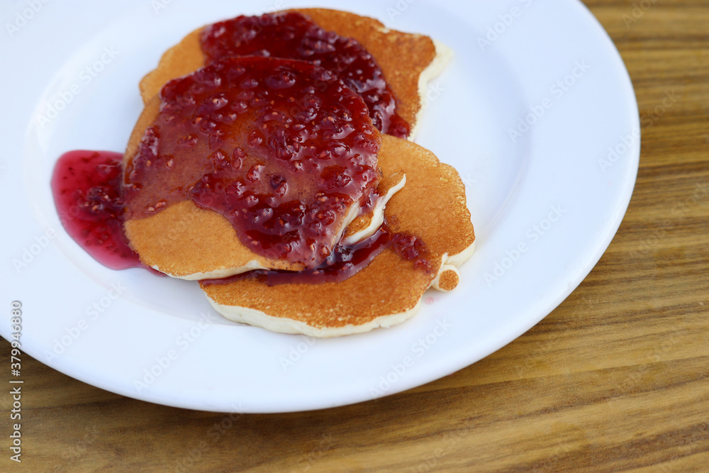 Pancakes drizzled with raspberry jam in a white plate on wooden table. Tasty dessert, sweet breakfast Pancakes drizzled with raspberry jam in a white plate on wooden table. Tasty dessert, sweet breakfast