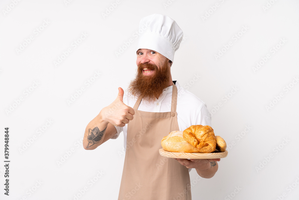 Redhead man in chef uniform. Male baker holding a table with several breads with thumbs up because something good has happened Redhead man in chef uniform. Male baker holding a table with several breads with thumbs up because something good has happened