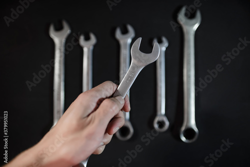 A man holds a steel wrench in his hand. Background set of wrenches for car repair. Car mechanic concept, car service. 