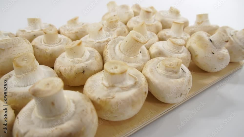 Champignon mushrooms on a wooden cutting board. Dolly shooting, white background. Champignon mushrooms on a wooden cutting board. Dolly shooting, white background.