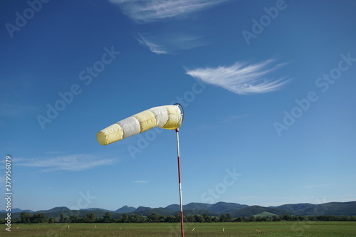 Yellow-white wind sock on the blue sky background.