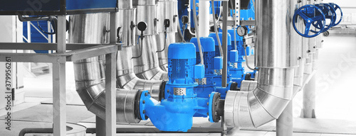 Modern industrial boiler room with pumps and pipe lines supplying steam with pressure gauges installed in. Blue toning. Panoramic banner.