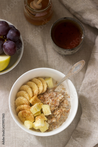 Buckwheat porridge with fruit, green tea, fruit and honey on a linen tablecloth. Rustic style.