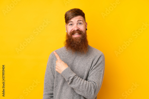 Redhead man with long beard over isolated yellow background pointing to the side to present a product