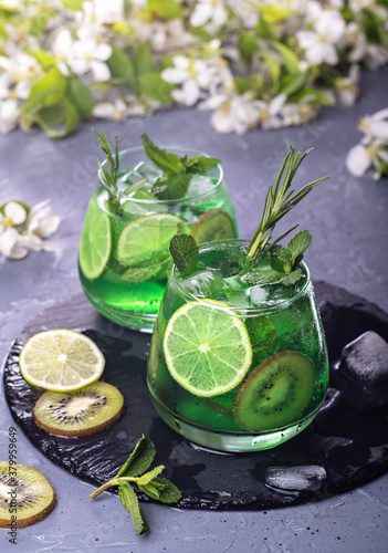 Non-alcoholic Mojito cocktail in a glass with syrup, fresh mint, lime and kiwi slices, sparkling water with ice. It has a citrus aroma and pleasant taste.