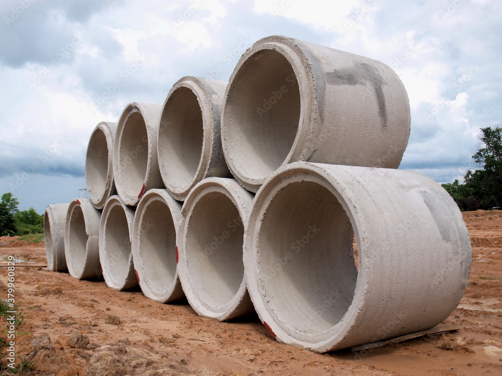 Concrete sewer piles on the ground. For the drainage system in the construction site. On the blue sky background there are white clouds. Focus close and choose the subject. Concrete sewer piles on the ground. For the drainage system in the construction site. On the blue sky background there are white clouds. Focus close and choose the subject.