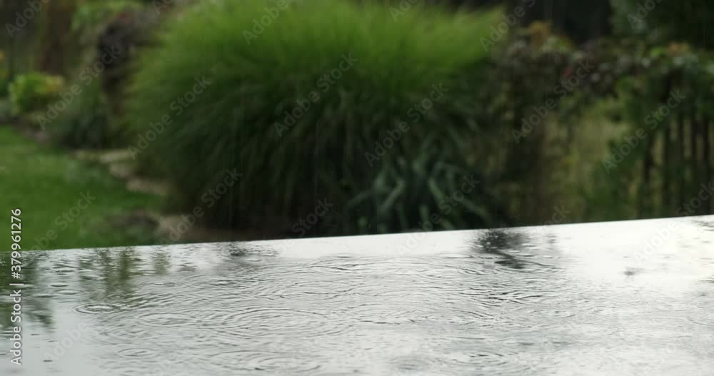 Close up of rain falling on a black table with a garden in the background. Close up of rain falling on a black table with a garden in the background.