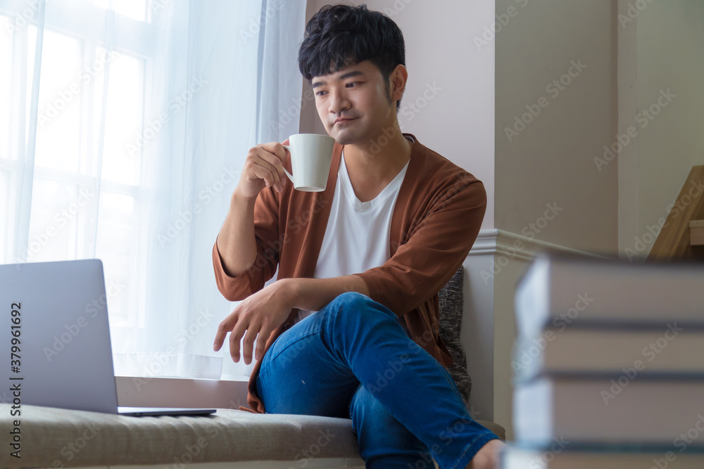 Portrait of an attractive smiling young man wearing casual clothes sitting beside window at home, using laptop computer. Portrait of an attractive smiling young man wearing casual clothes sitting beside window at home, using laptop computer.