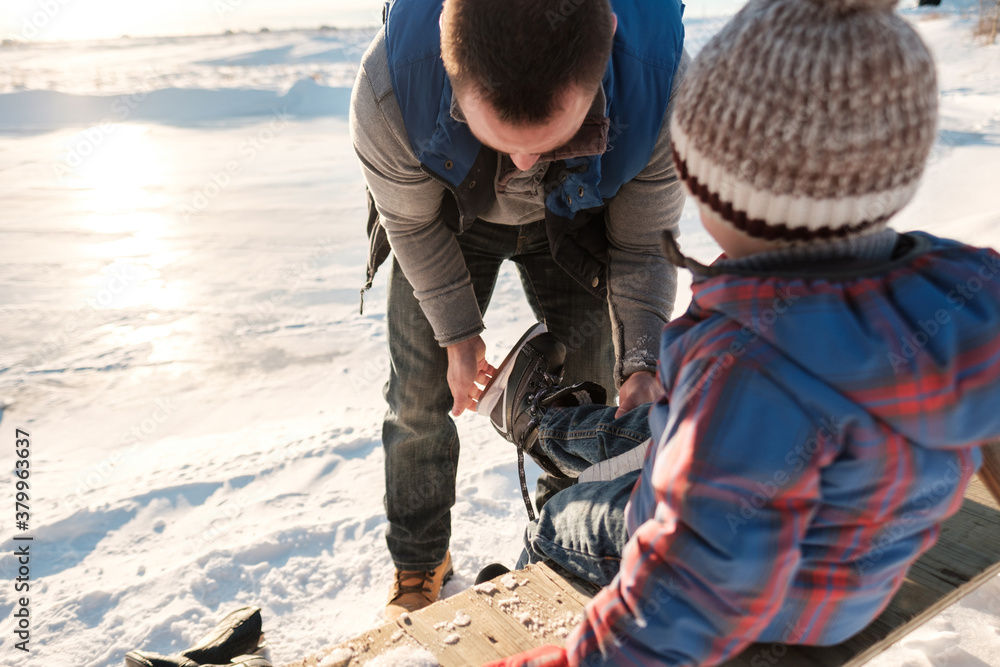 A father ties his son's skates at an frozen pond. A father ties his son's skates at an frozen pond.