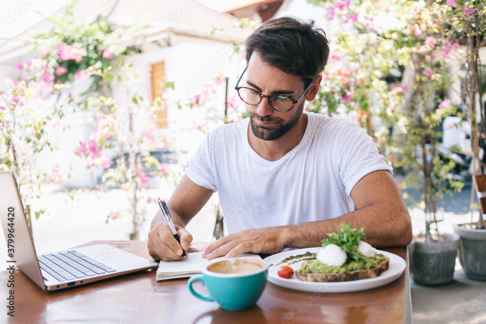 Focused man writing in notebook during breakfast Focused man writing in notebook during breakfast