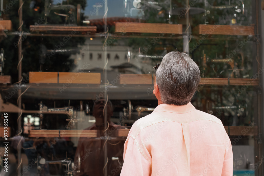 old Man with white hair looking at old sewing machines through a storefront window 