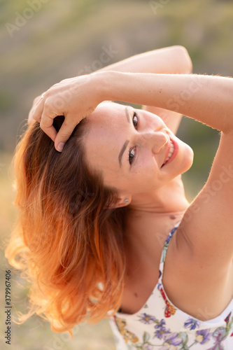 Tender beautiful red-haired girl enjoys the sunset in a field with a hill.