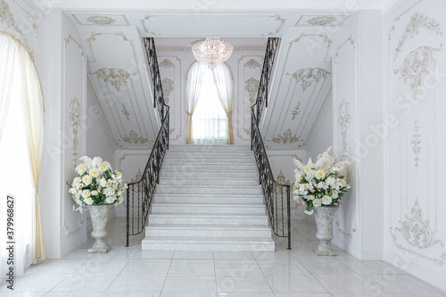 luxury royal posh interior in baroque style. very bright, light and white hall with expensive oldstyle furniture. chic wide marble staircase leading to the second floor
