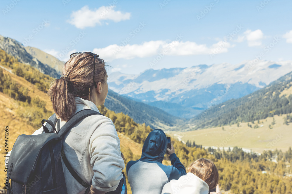Fototapeta premium A group of tourists gaze at the impressive mountain landscape and take photos on a sunny autumn day. Russia, Arkhyz