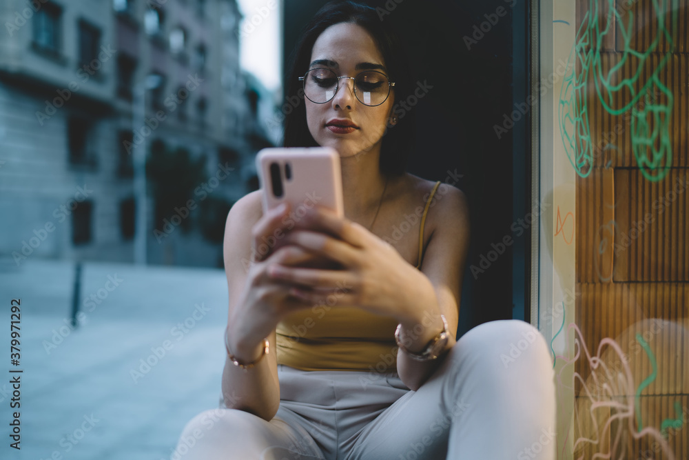 Obraz premium Young woman chatting via smartphone on street windowsill