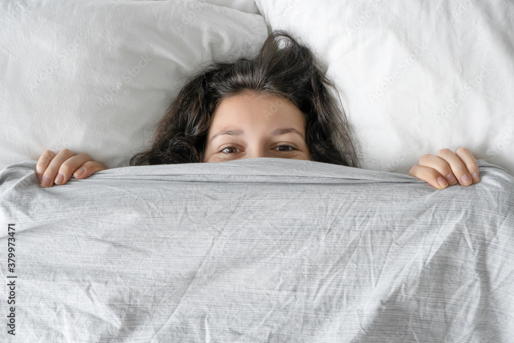 The girl does not want to get out of bed in the morning. Hiding in a blanket. View from above. Ambush in bed The girl does not want to get out of bed in the morning. Hiding in a blanket. View from above. Ambush in bed