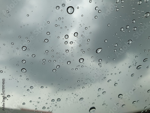 Raindrops dripping by the window of a car driving on the road, while it is cloudy and rainy in the evening. 