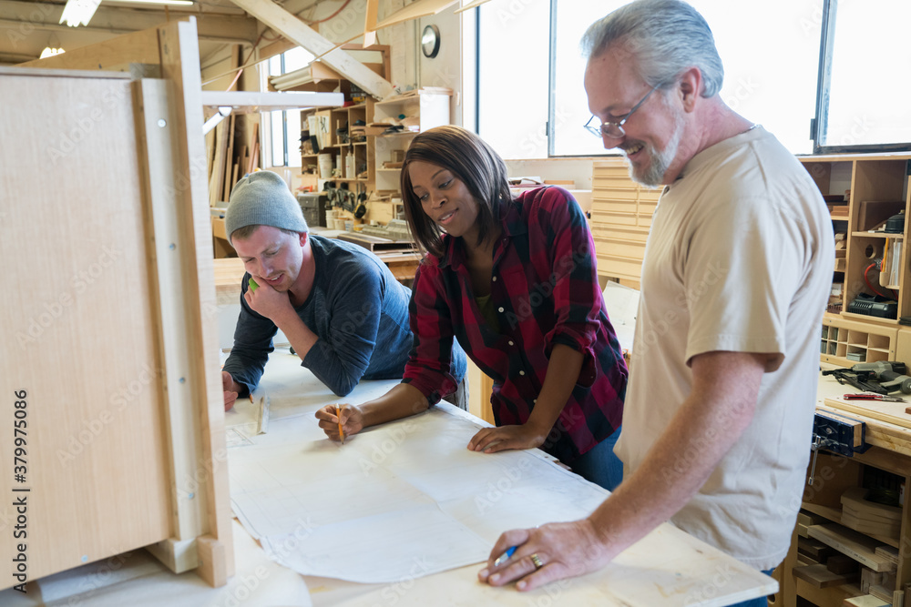 Three cabinet shop workers going over blueprints Three cabinet shop workers going over blueprints