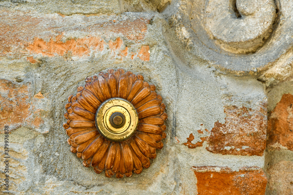 Close-up of an old terracotta doorbell in the shape of a flower on a weathered brick and stone wall, Italy