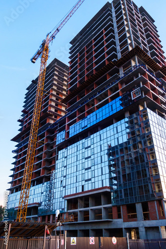 A crane at a high-rise building under construction. The construction site is fenced with warning signs attached to it.