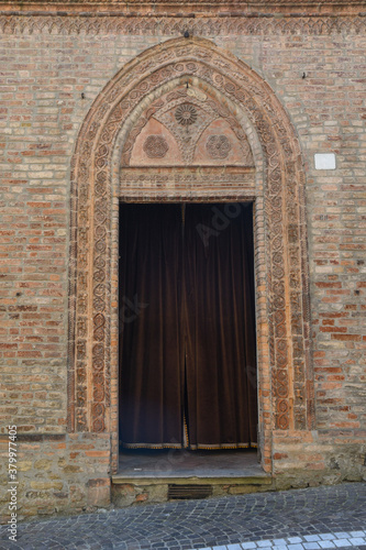Close-up of the old entrance portal of a medieval church with a decorated brick frame and a velvet curtain  Italy