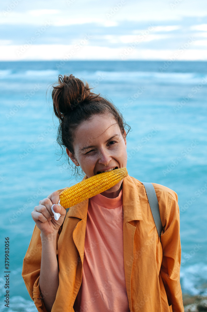 Young woman enjoying grilled corn on the ocean background Young woman enjoying grilled corn on the ocean background