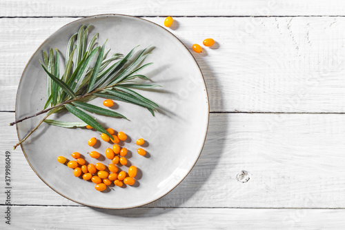 Green branch and fresh sea buckthorn berries on a plate on a white wooden table photo