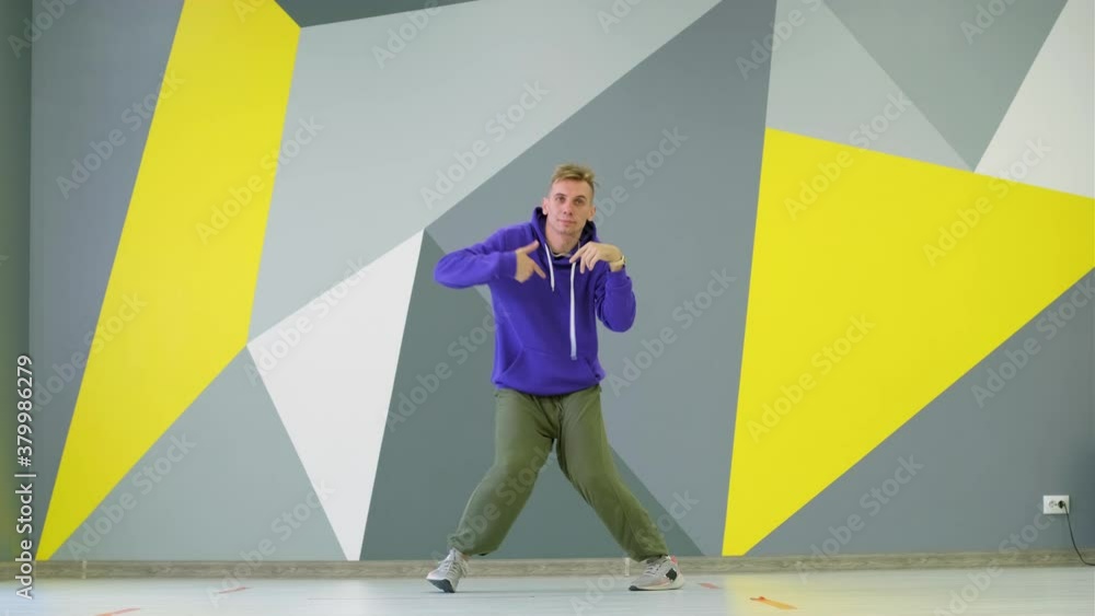 Energetic guy dancing hip hop, modern dance free style in a dance studio in front of the wall with bright geometric pattern. Energetic guy dancing hip hop, modern dance free style in a dance studio in front of the wall with bright geometric pattern.