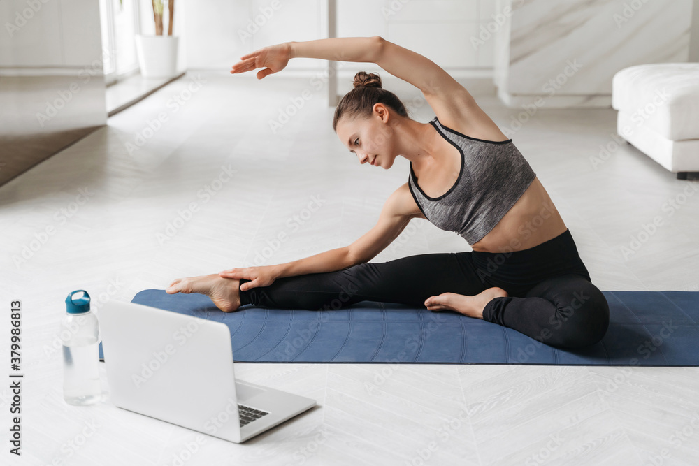 Young sporty woman exercising while sitting on yoga mat in her