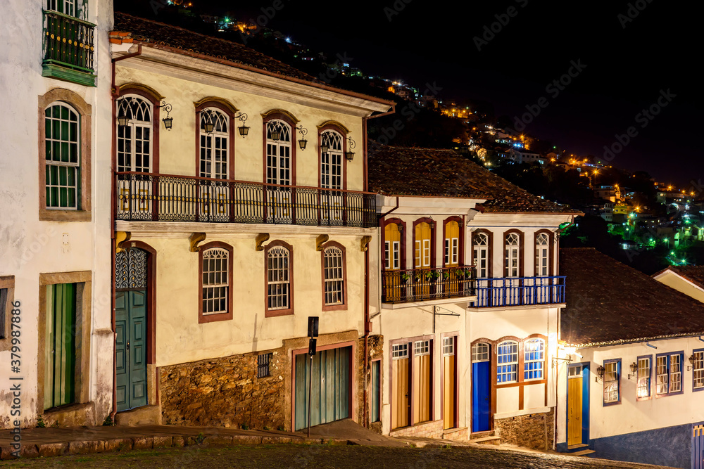 Obraz premium Facades of houses in colonial architecture on an old cobblestone street in the city of Ouro Preto illuminated at night