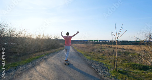 Young male ride on longboard skateboard on the country road in sunny day 