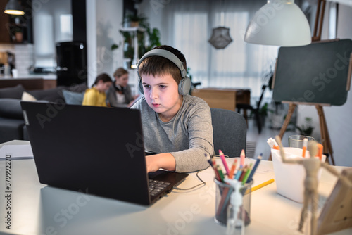 Cute boy with headphones using laptop computer for online learning. Home school. Child doing homework at home. Lifestyle concept for home schooling. Social distancing and education.