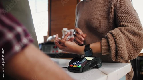 Customer paying with NFC technology by smart watch contactless on terminal in modern cafe, barman woman in medical mask, business reopen after covid coronavirus lockdown