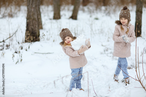 little girls play in the winter forest and make snow balls for the snowman. walking in any weather. new year vacations. happy childhood.