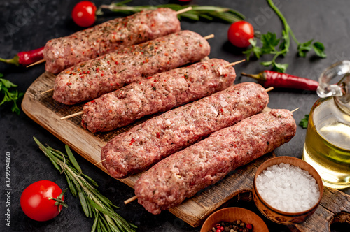 raw Lula kebab  on skewers with spices on a stone background 