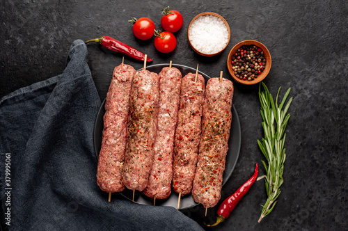 raw Lula kebab on skewers with spices in a black plate on a stone background