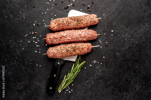 raw Lula kebab on skewers with spices over a meat knife on a stone background