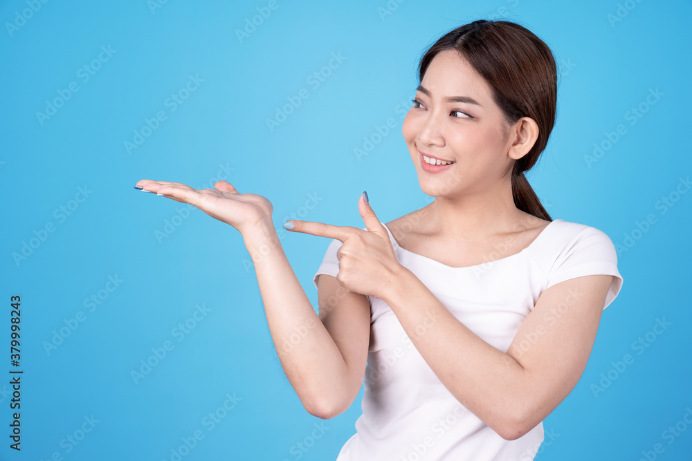 Asian model pointing fingers at an empty space next to her, Isolated on a blue background. Asian model pointing fingers at an empty space next to her, Isolated on a blue background.
