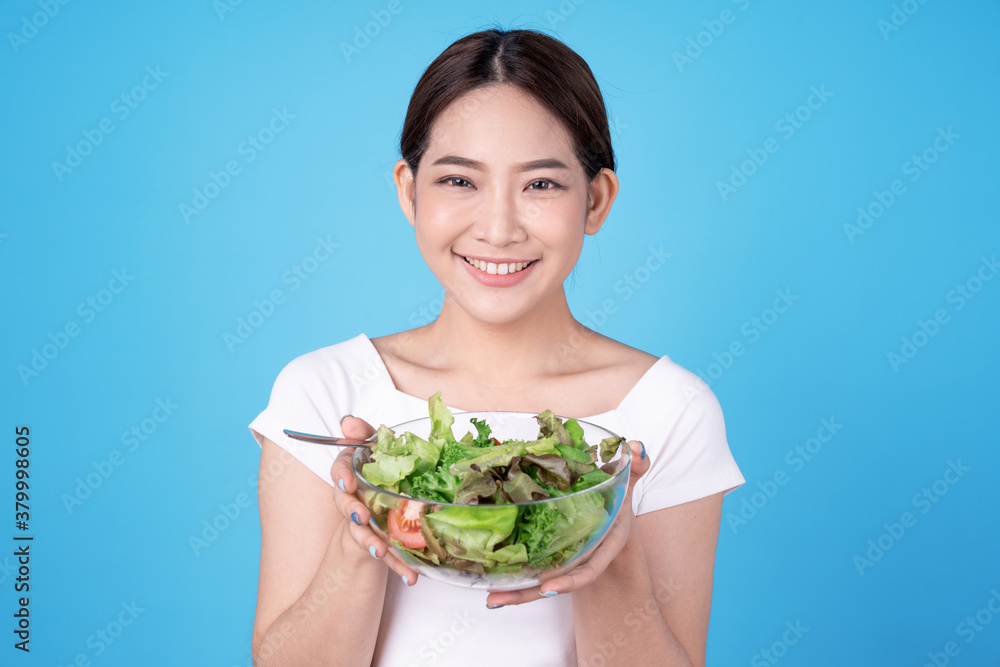 Happy Asian woman eating a fresh salad from a bowl, Isolated on blue background. Happy Asian woman eating a fresh salad from a bowl, Isolated on blue background.