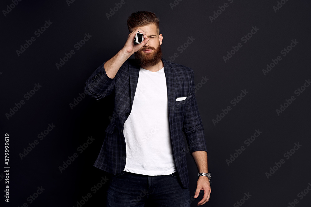 Confident businessman with ginger beard standing on a black background holding a newspaper near his face like a spyglass Confident businessman with ginger beard standing on a black background holding a newspaper near his face like a spyglass