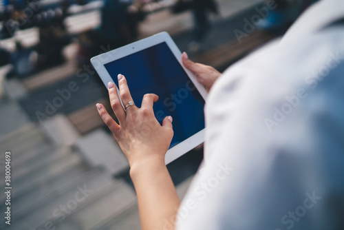 Crop woman touching screen of tablet on street at daytime