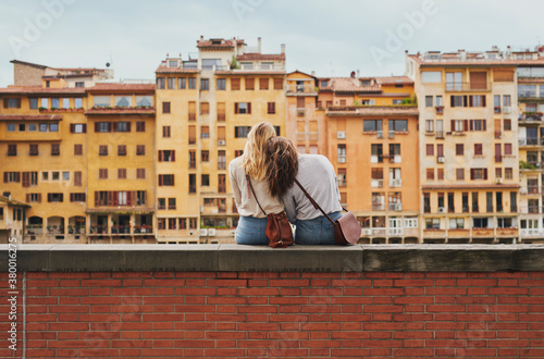 Two tourist girl friends relaxing on historical bridge in Floren