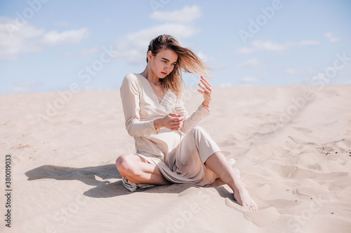 A young, slender girl in a beige dress poses in the wind in the desert © Denis