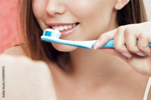 A young woman is brushing teeth in the bathroom. Reflection in the mirror