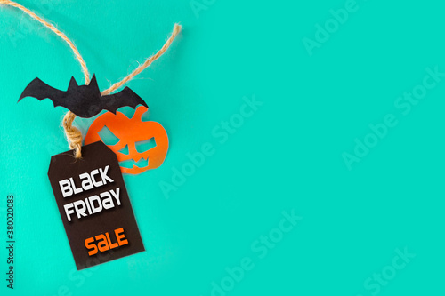 Black Friday and Halloween concept. Black Friday sale tag with bat and jack pumpkin on turquoise with copy space for text or ad photo