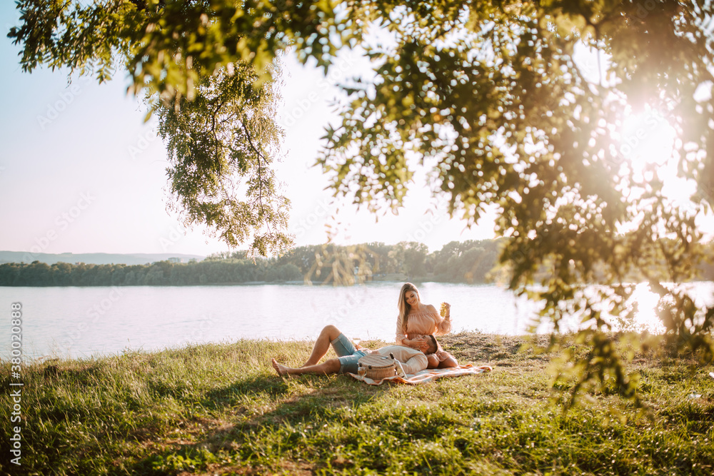 Attractive blonde caucasian woman and caucasian man lying on the beach at sunset. A loving couple on a picnic by the river Attractive blonde caucasian woman and caucasian man lying on the beach at sunset. A loving couple on a picnic by the river