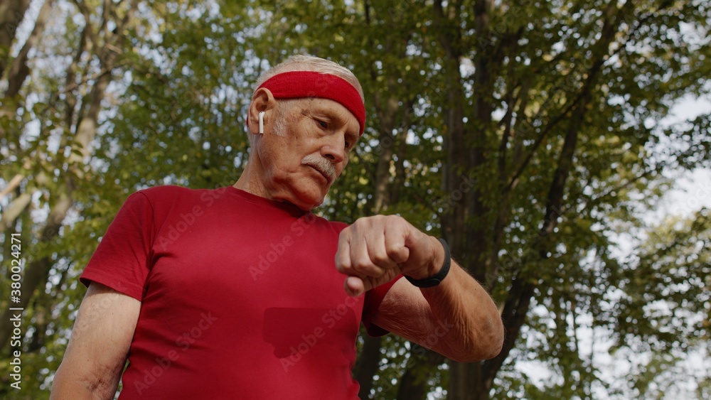 Senior runner man in park using smart watch, tracking distance, checking pulse after fitness workout Senior runner man in park using smart watch, tracking distance, checking pulse after fitness workout