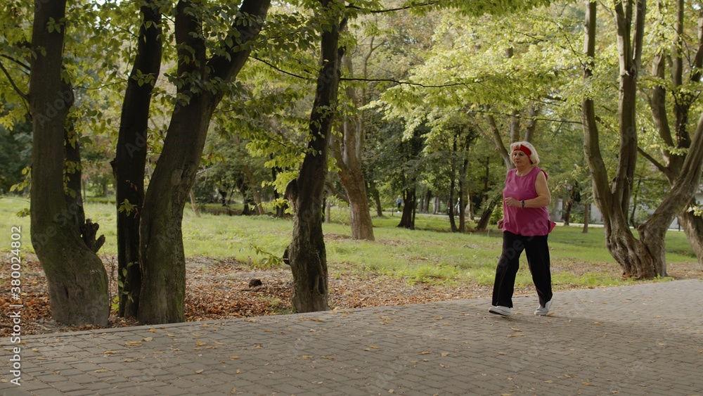Senior old woman running in park and using smart watch. Female runner working out cardio outdoor Senior old woman running in park and using smart watch. Female runner working out cardio outdoor